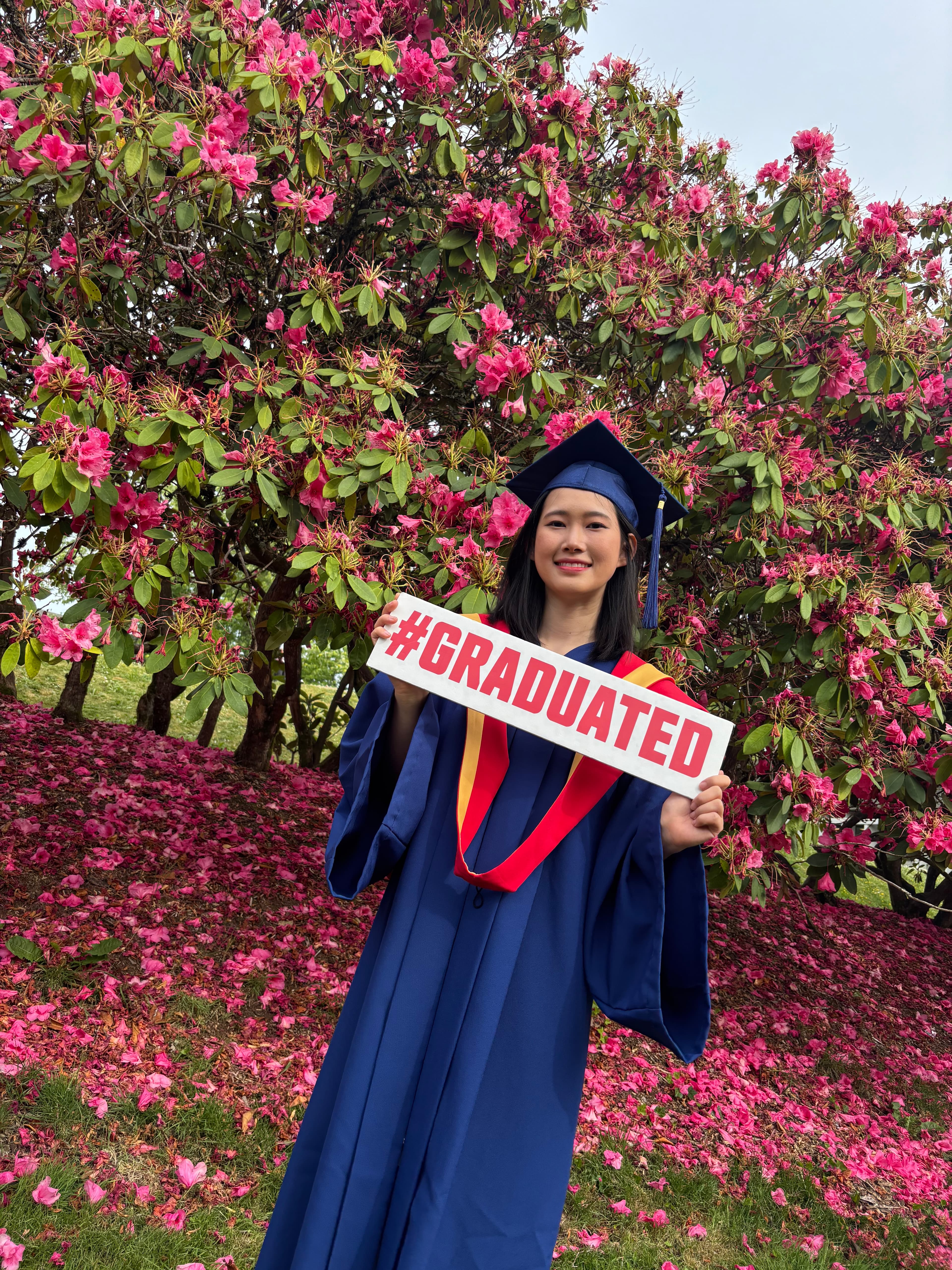 Reina celebrating graduation in front of flowering bushes
